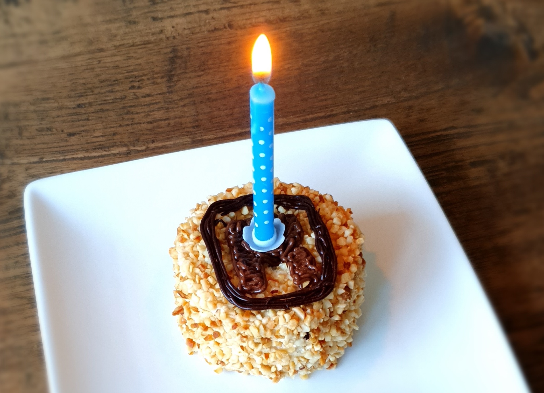 Pastry with the logo of this website and one burning candle on it